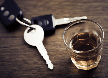 set of car keys on a dark wood table next to a glass of alcohol