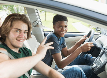 Two young teenagers in the drivers seat and passenger seat of a car